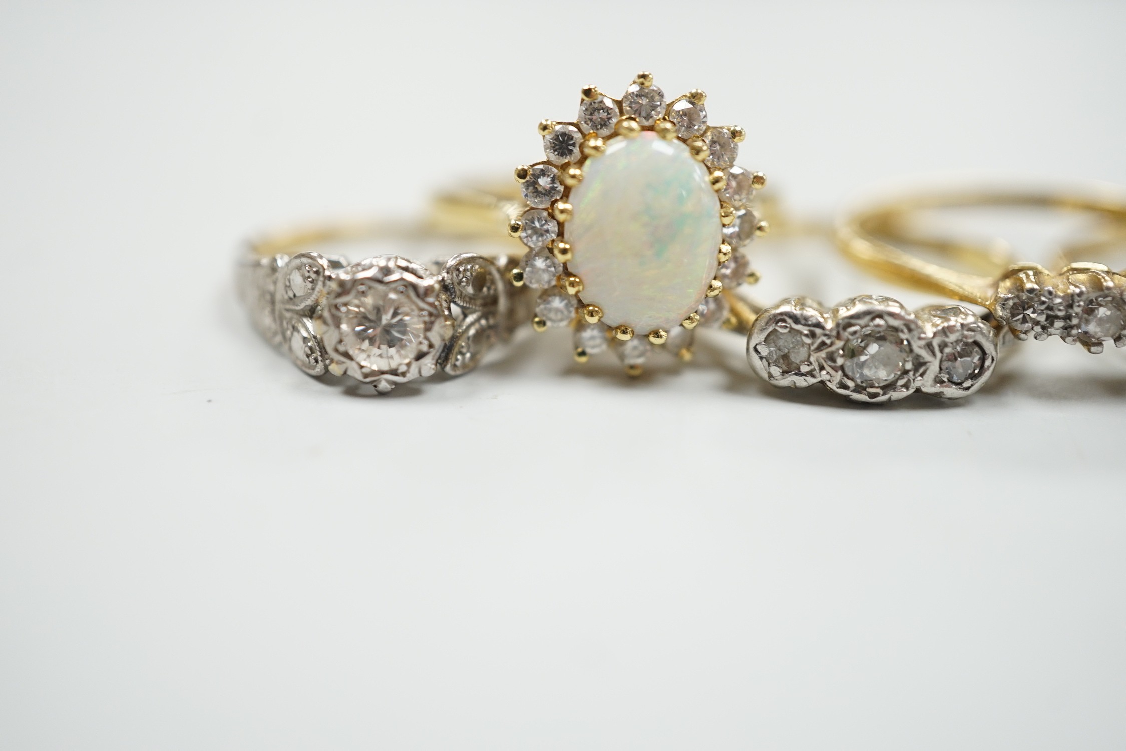 Four assorted 18ct and gem set dress rings, including white opal and diamond and two three stone diamond and one yellow metal and single stone diamond set ring, gross weight 14.3 grams.